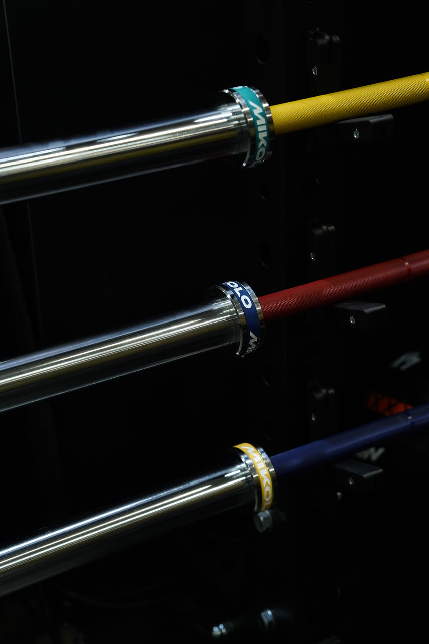 Three barbells with chrome sleeves and yellow, red, and blue shafts resting on a black rack