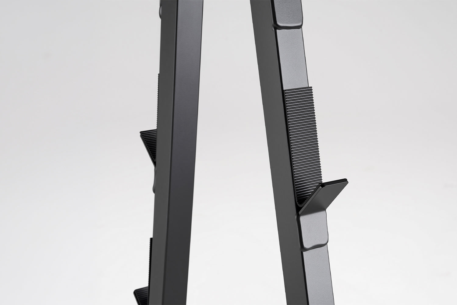 Two dark grey vertical metal posts with adjustable, ribbed hooks for a barbell rack against a white background