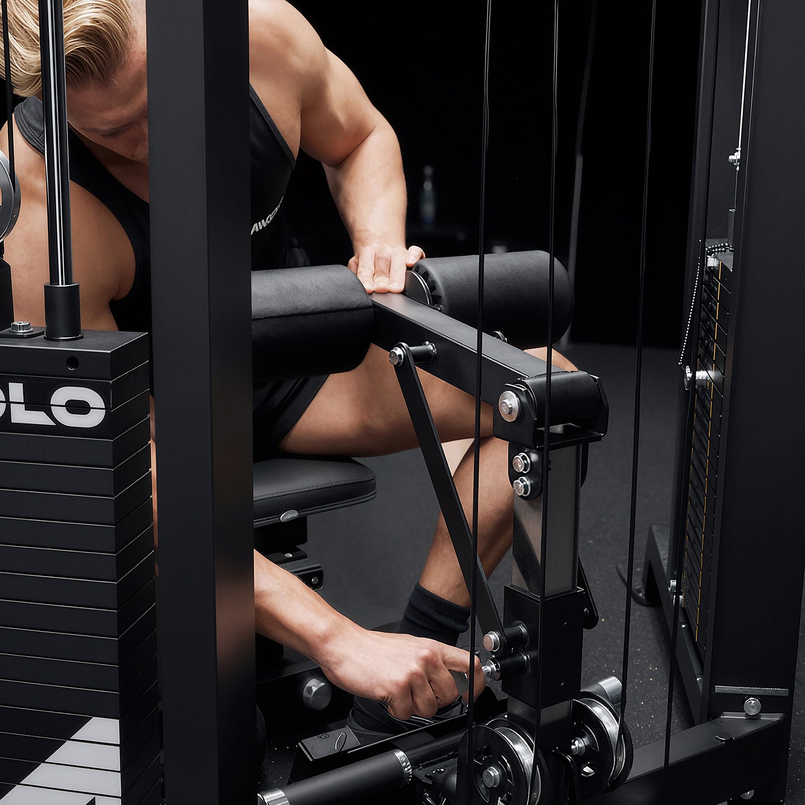 Close-up of adjusting the padded lat pulldown leg roller hold-down on the Mikolo FALCON™-2.0