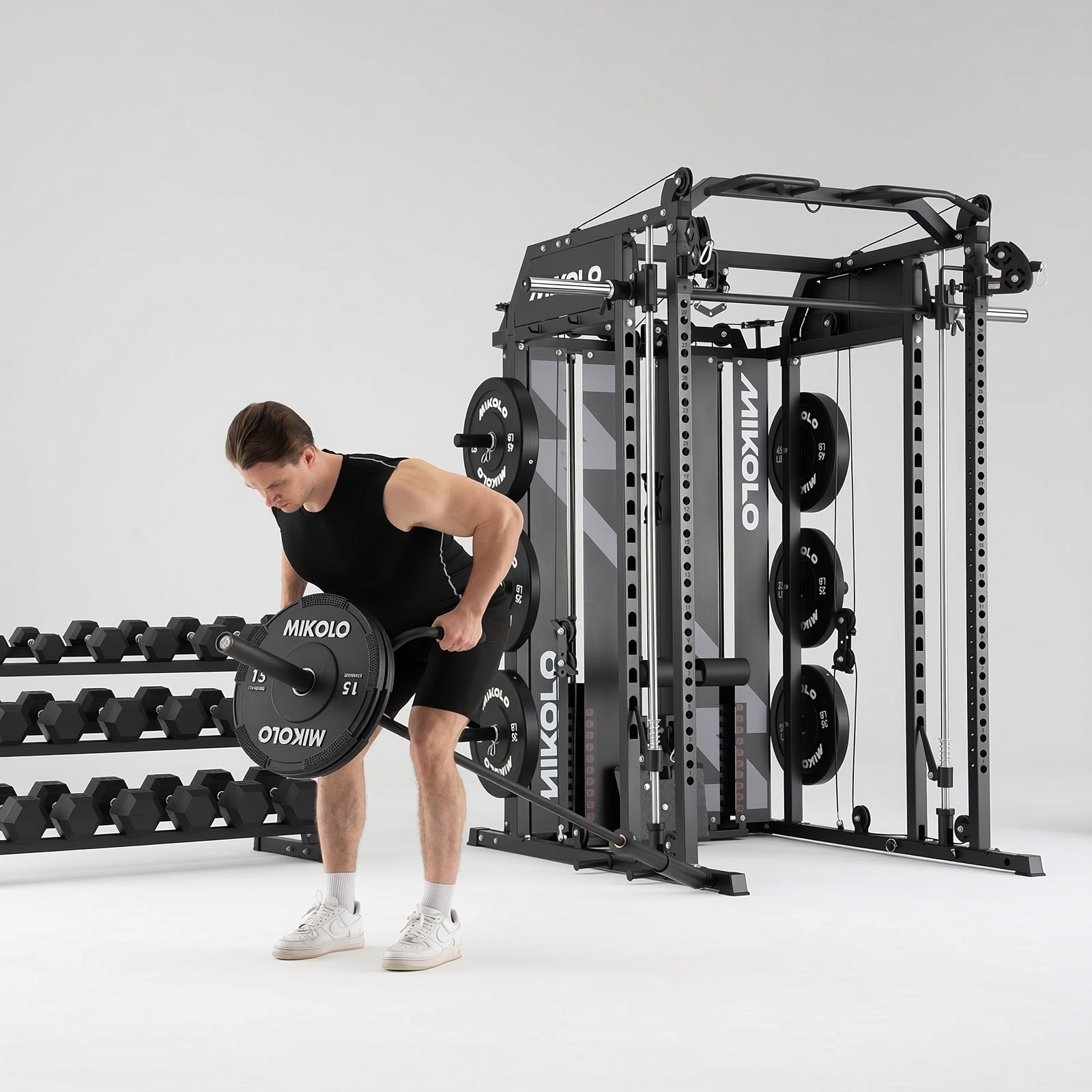 Man performing a row exercise with a barbell on a black Mikolo Smith machine and functional trainer next to a dumbbell rack