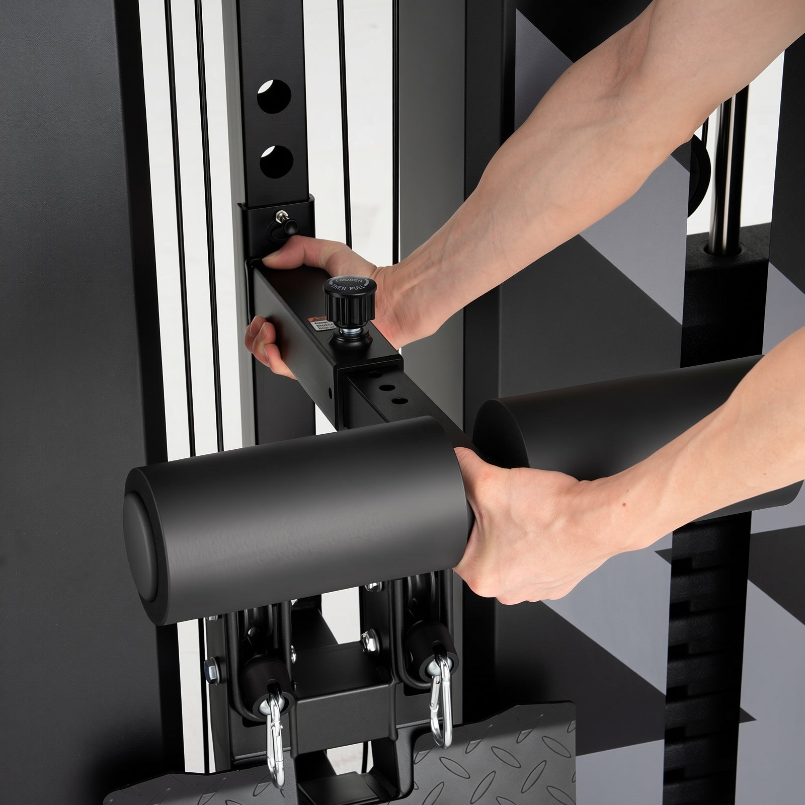 Person adjusting a black padded bar attachment on a gym machine, turning a knob to lock it into a vertical rail