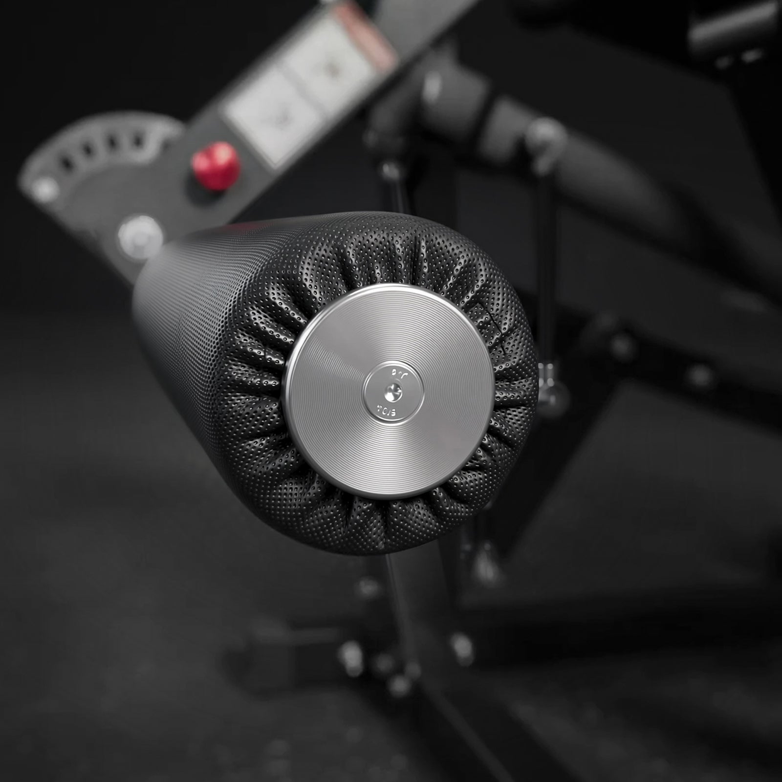 Black perforated padded roller on a leg exercise machine with a silver circular metal end cap
