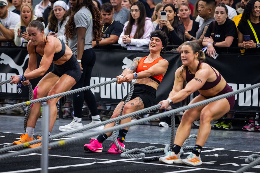 Three female athletes straining to pull thick ropes during a fitness competition in front of a crowd