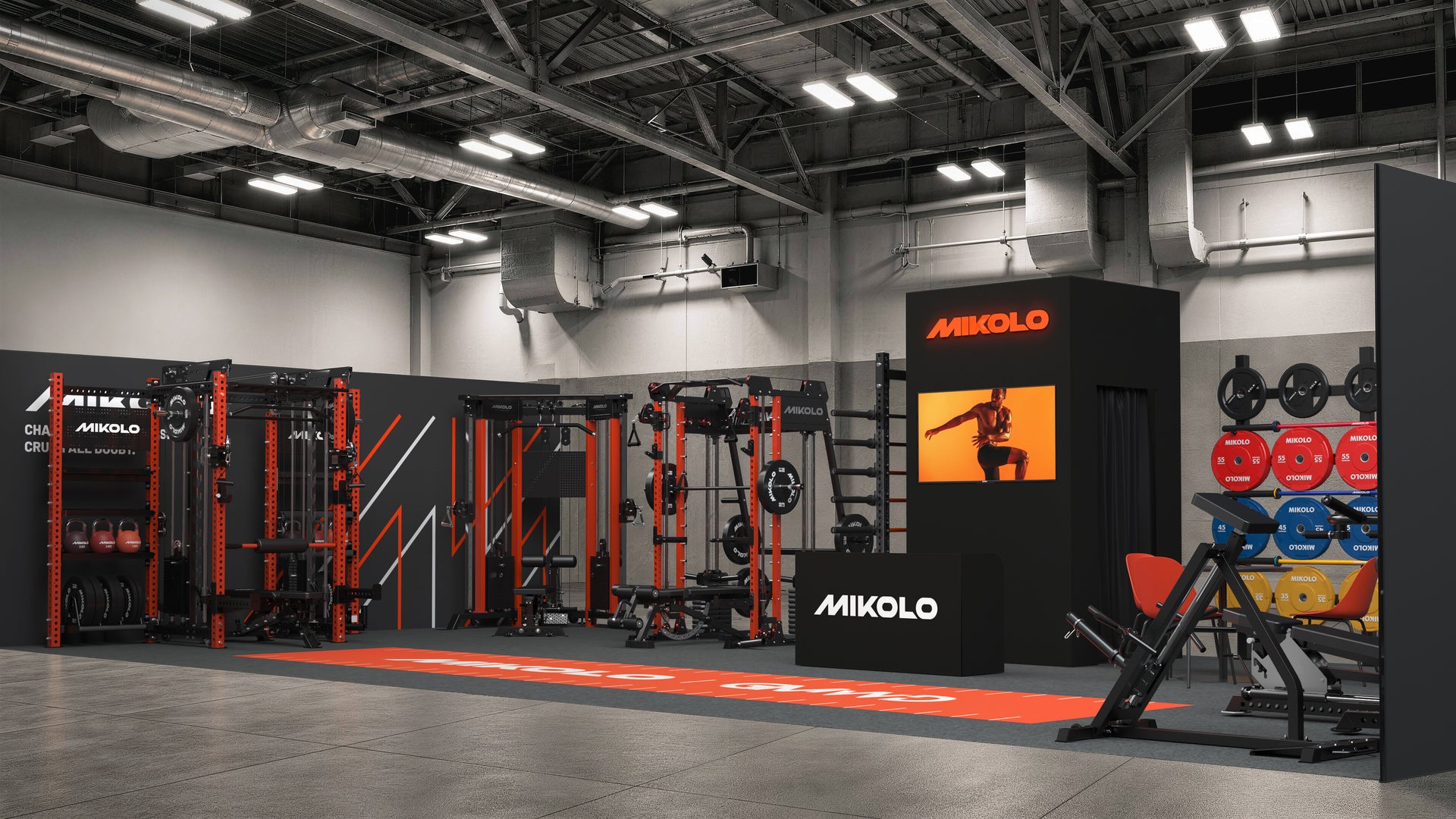Gym showroom with red and black MIKOLO equipment including squat racks, cable machines, weight plates, and a branded kiosk