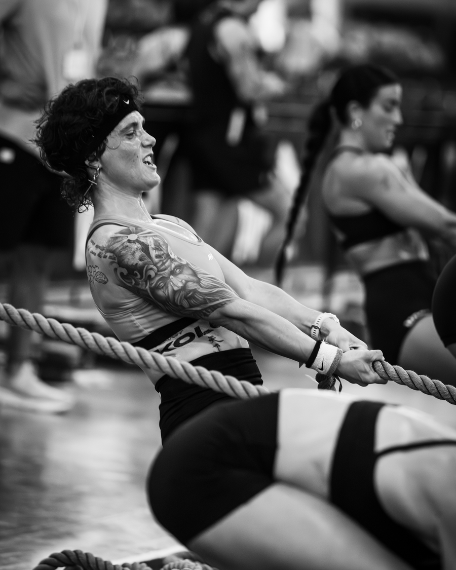 Woman with short curly hair and arm tattoo leaning back while pulling a thick rope during a workout