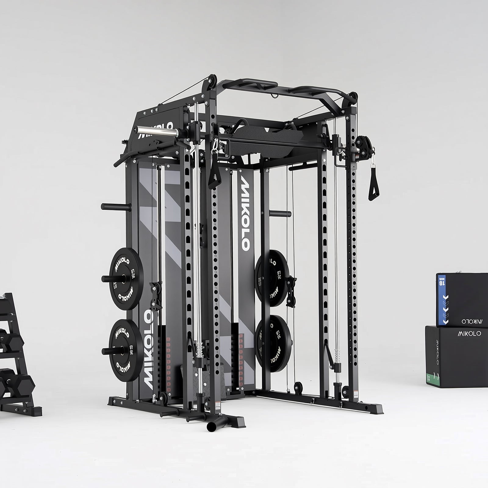 Black Mikolo Smith machine and functional trainer with weight plates, cables, and pull-up bar, next to dumbbells and plyo box