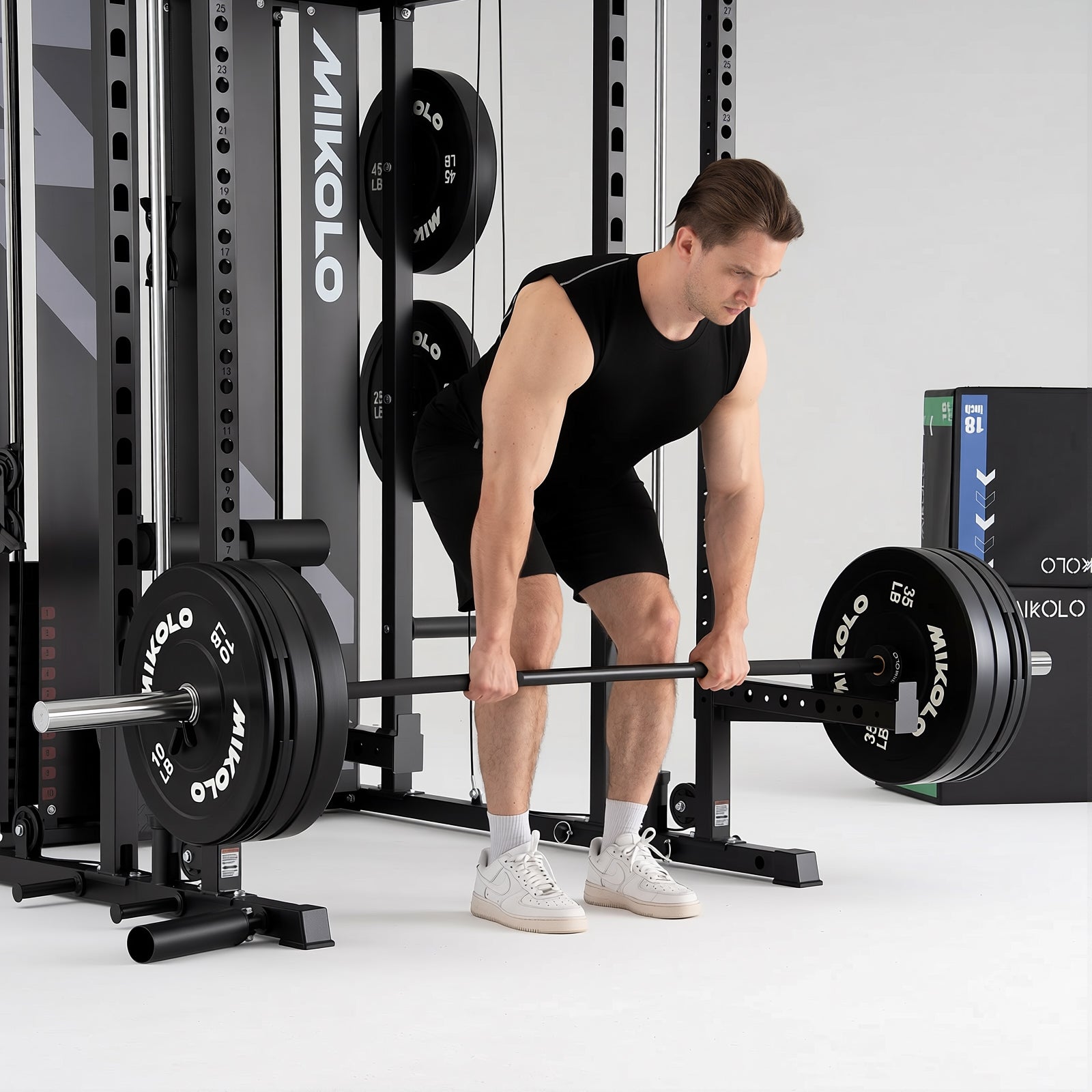 Muscular man in black workout gear performing a bent-over barbell row inside a black Mikolo power rack