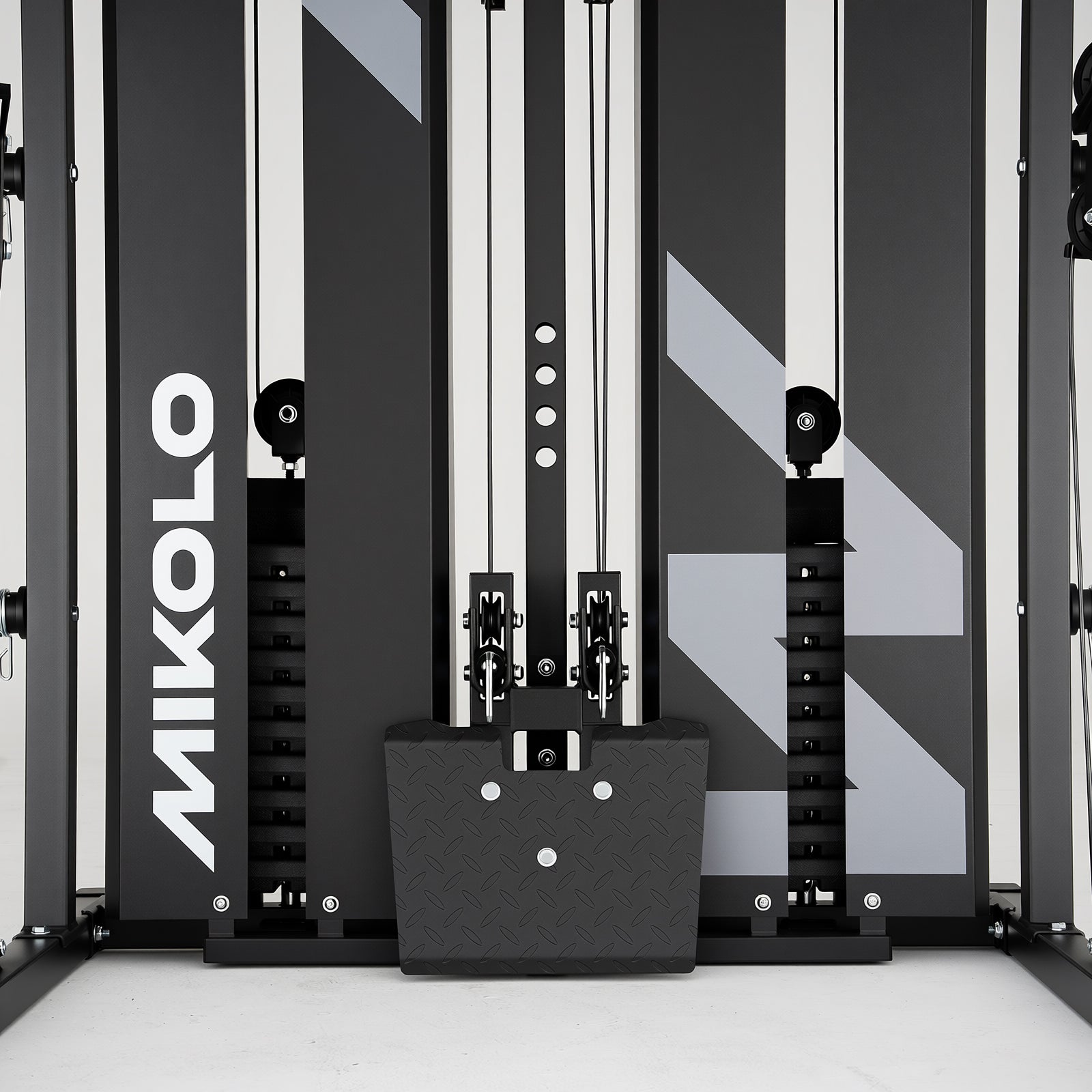 Vertical black panels with white Mikolo logo, dual weight stacks, cables, and a textured footplate at the bottom center