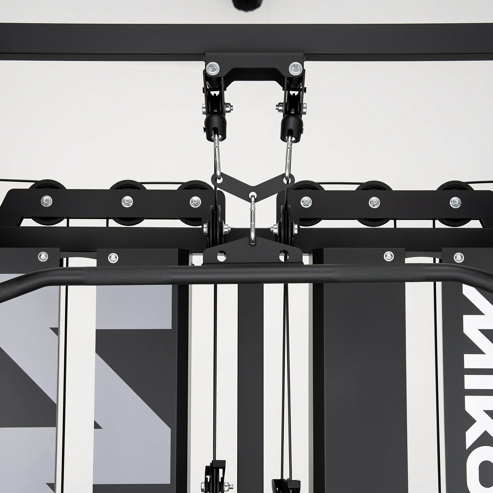 Black gym machine pulley system with cables, a V-bar attachment, and a textured pull-up bar above weight stacks