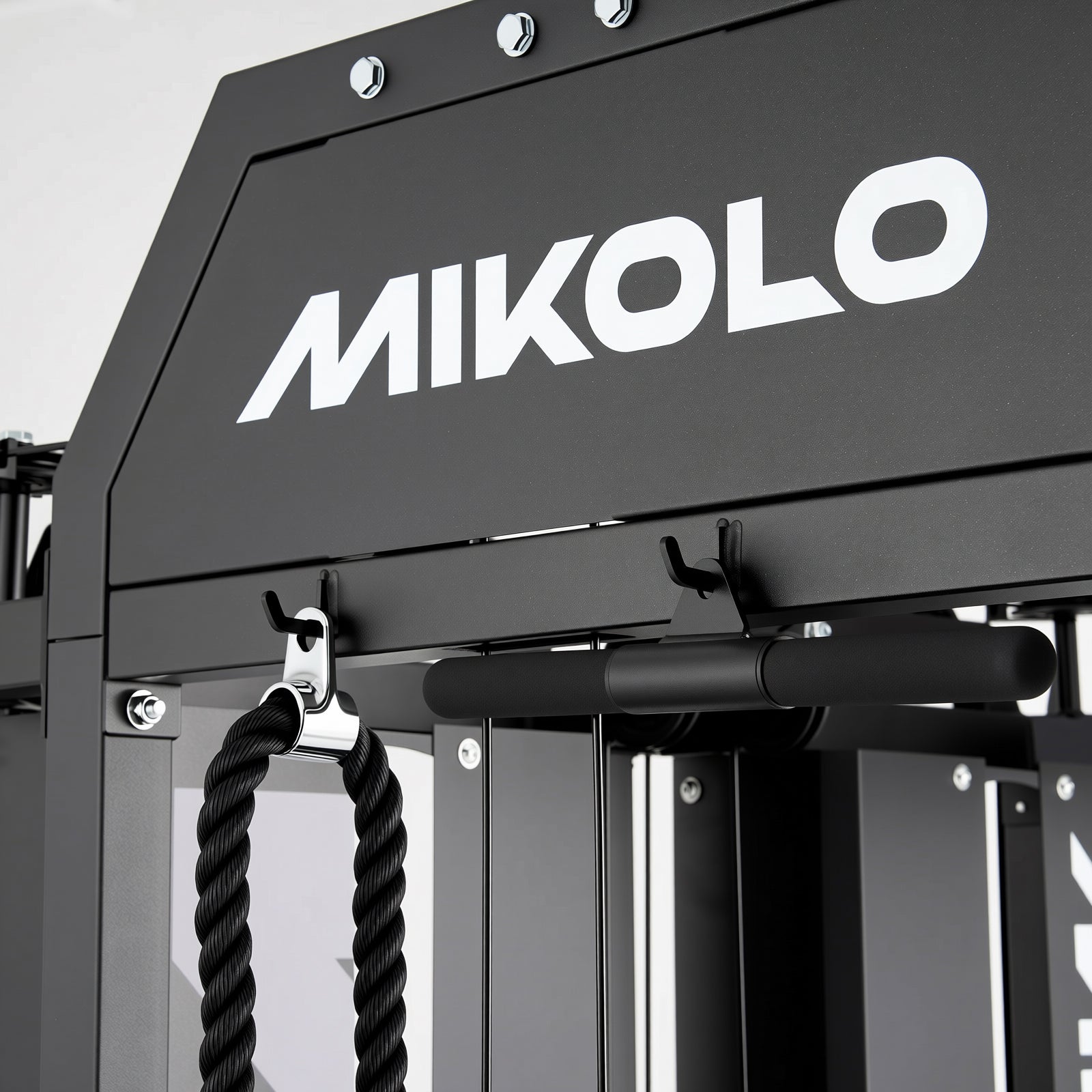 Close-up of black Mikolo gym machine frame with white logo, hooks holding a rope attachment and a bar
