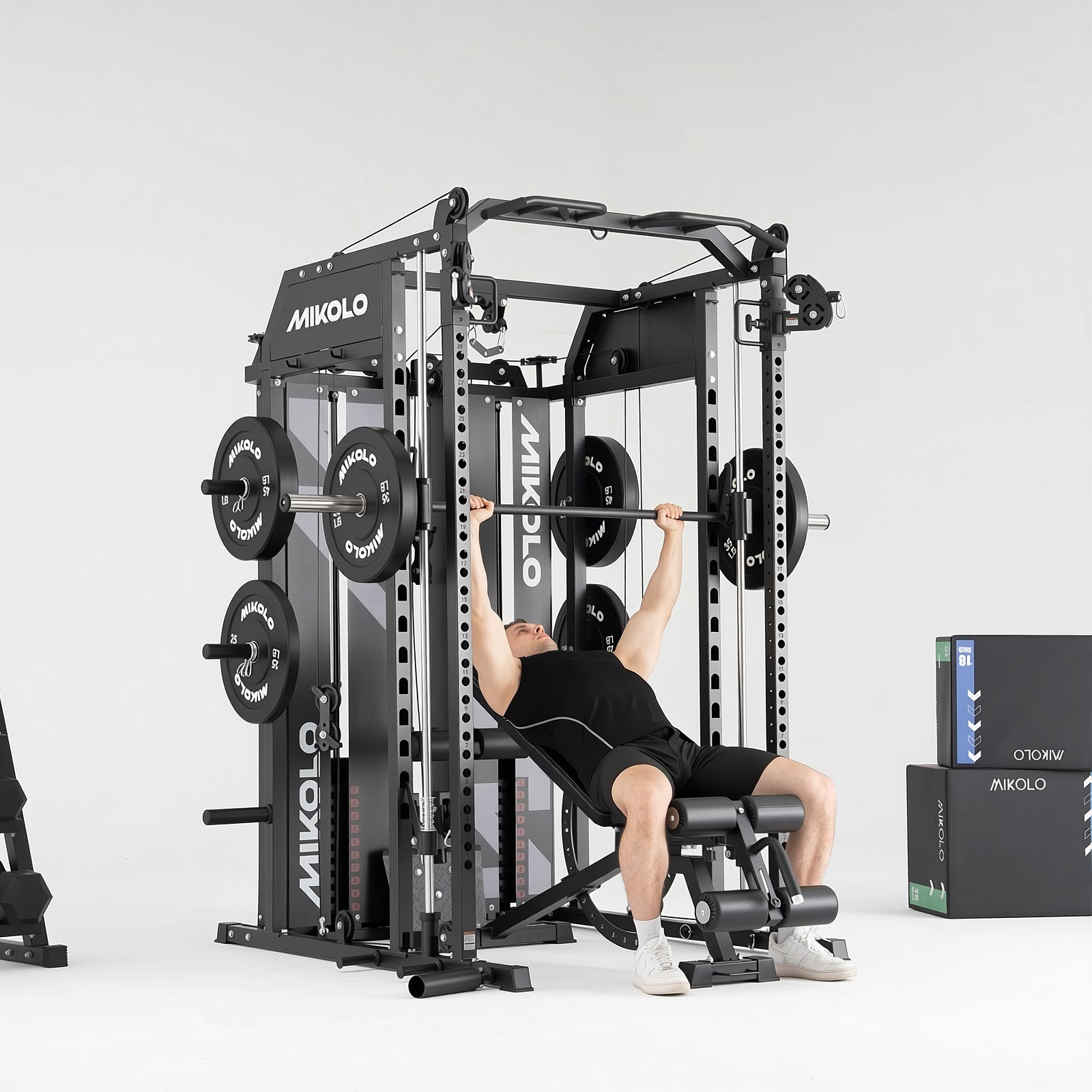 Man performing incline bench press on a black MIKOLO Smith machine functional trainer with weight plates and boxes