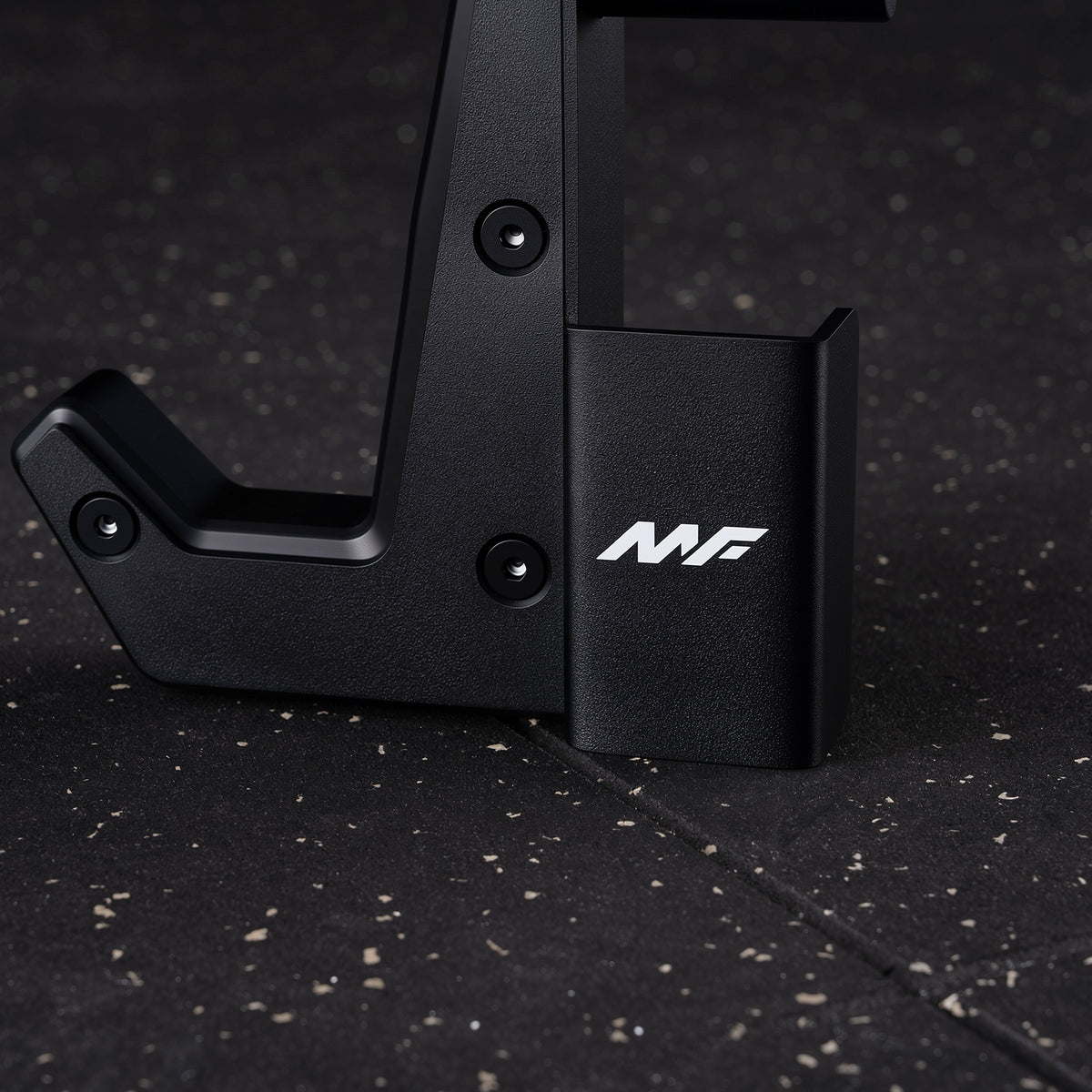 Black metal rack frame with a J-hook and storage cup displaying a white MF logo on a speckled gym floor