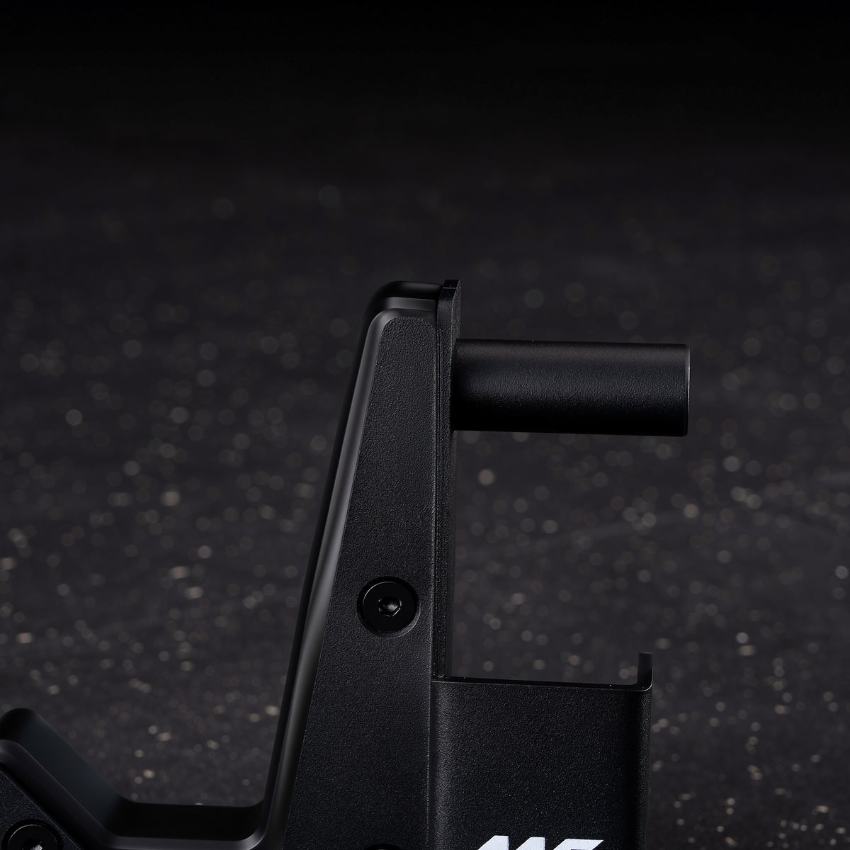 Black metal J-hook attachment with a vertical support, visible bolt, and horizontal cylindrical peg against a dark speckled f