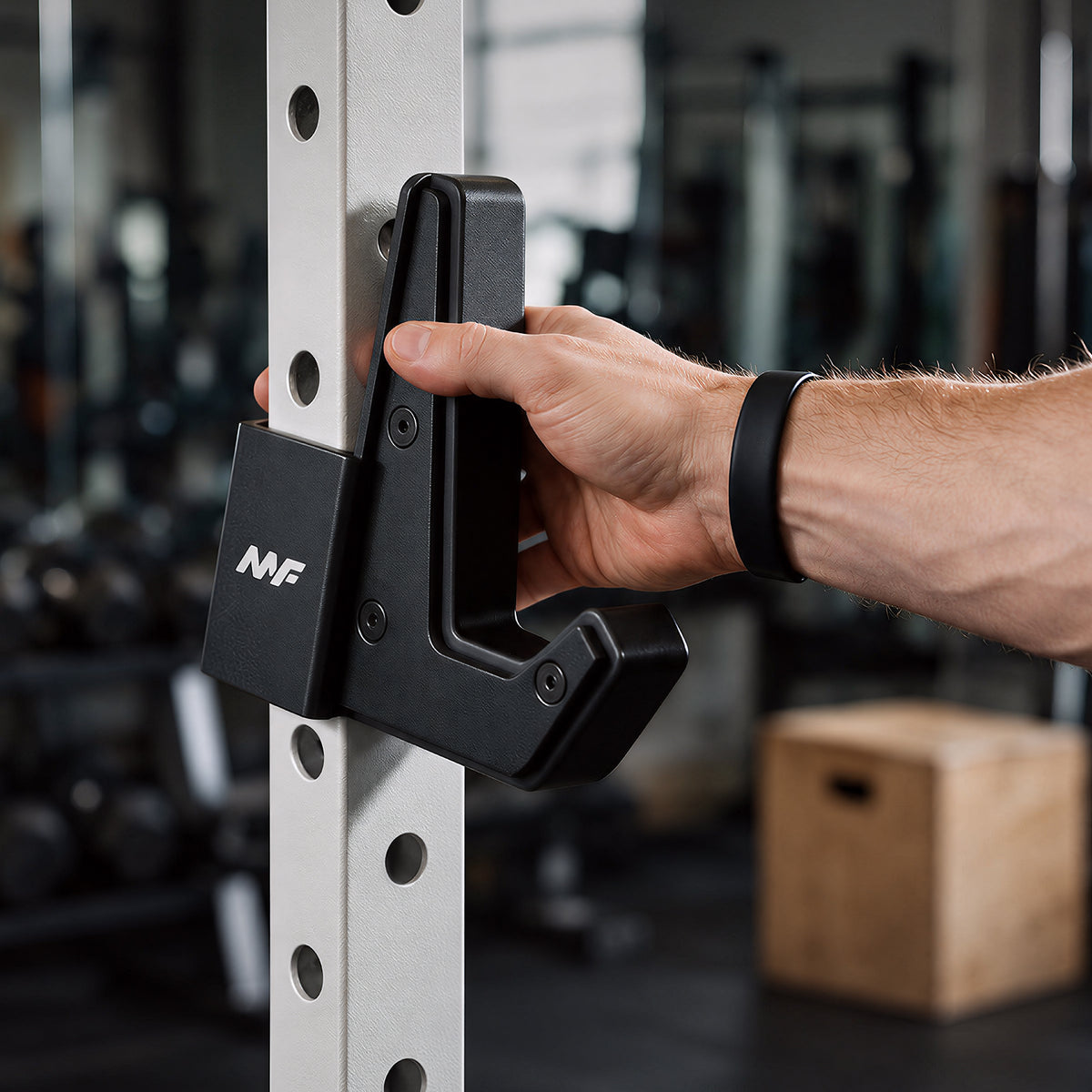 A hand adjusts a black J-hook attachment on a white perforated power rack upright