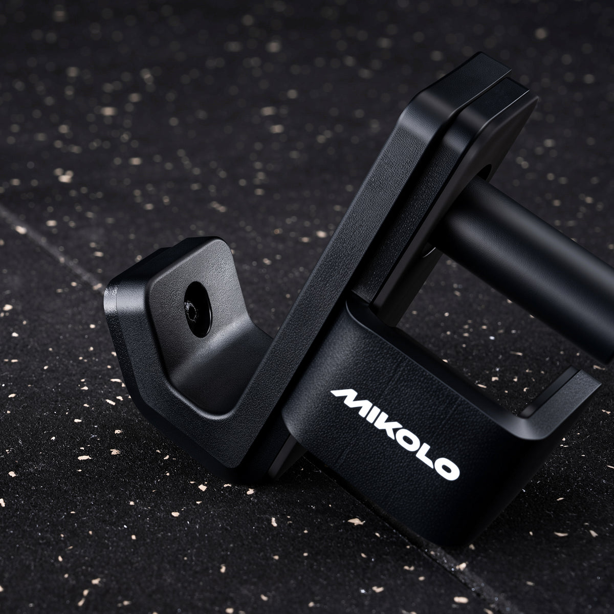 Black Mikolo J-hook barbell holder resting on a speckled rubber gym floor