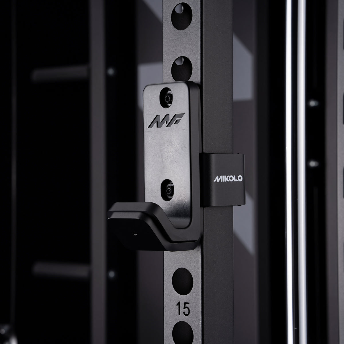 Black Mikolo J-hook attachment mounted on a power rack upright featuring a U-shaped barbell holder and branded side clamp