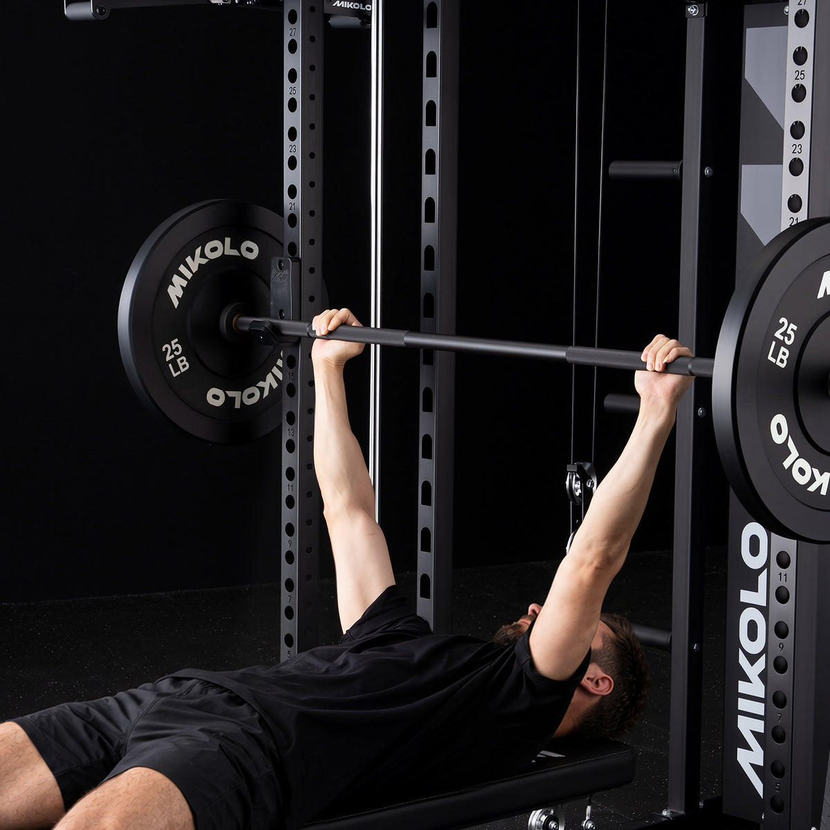 Man performing a bench press lifting a barbell with 25 lb MIKOLO weight plates inside a black power rack