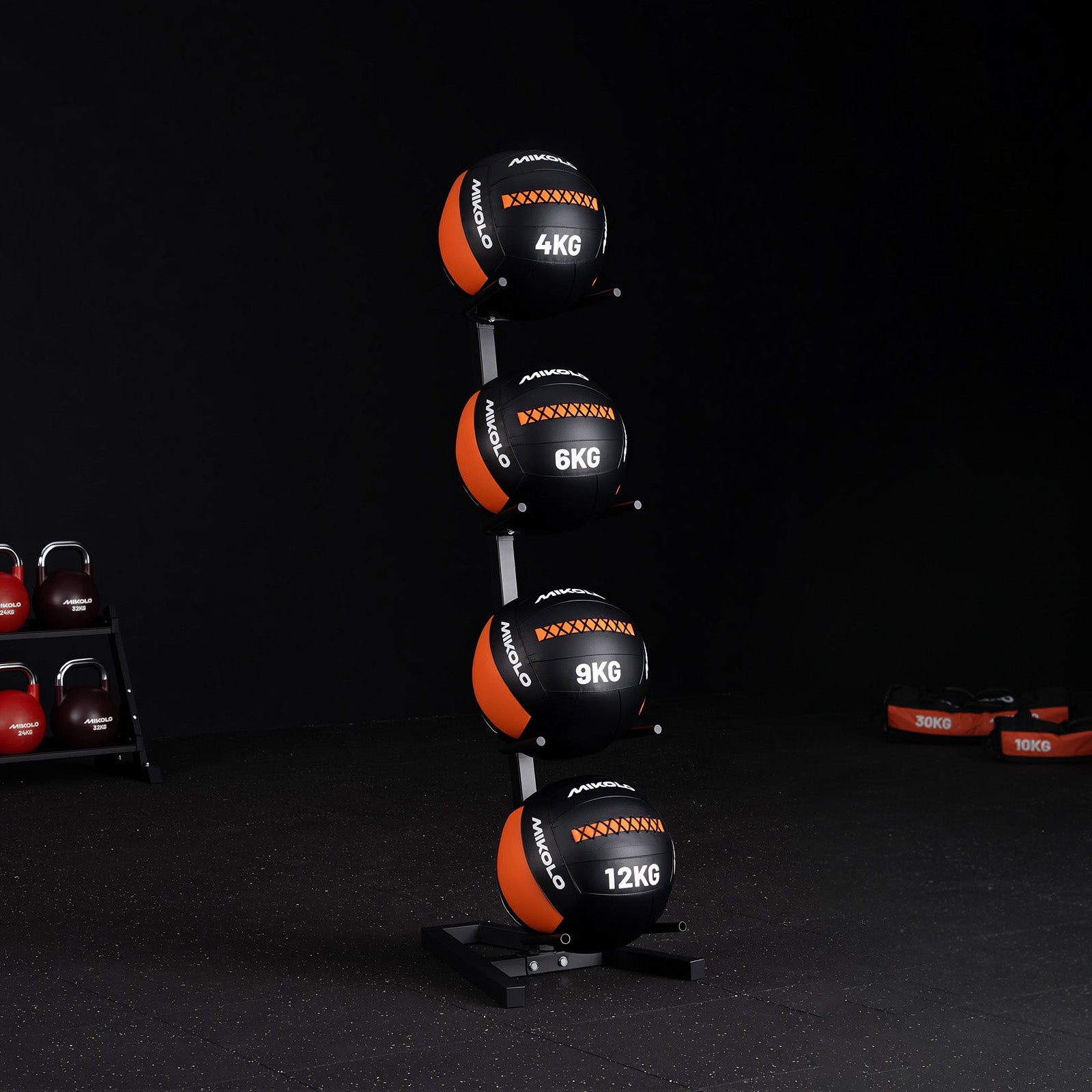 Vertical rack holding four black and orange Mikolo medicine balls labeled 4kg, 6kg, 9kg, and 12kg on a gym floor