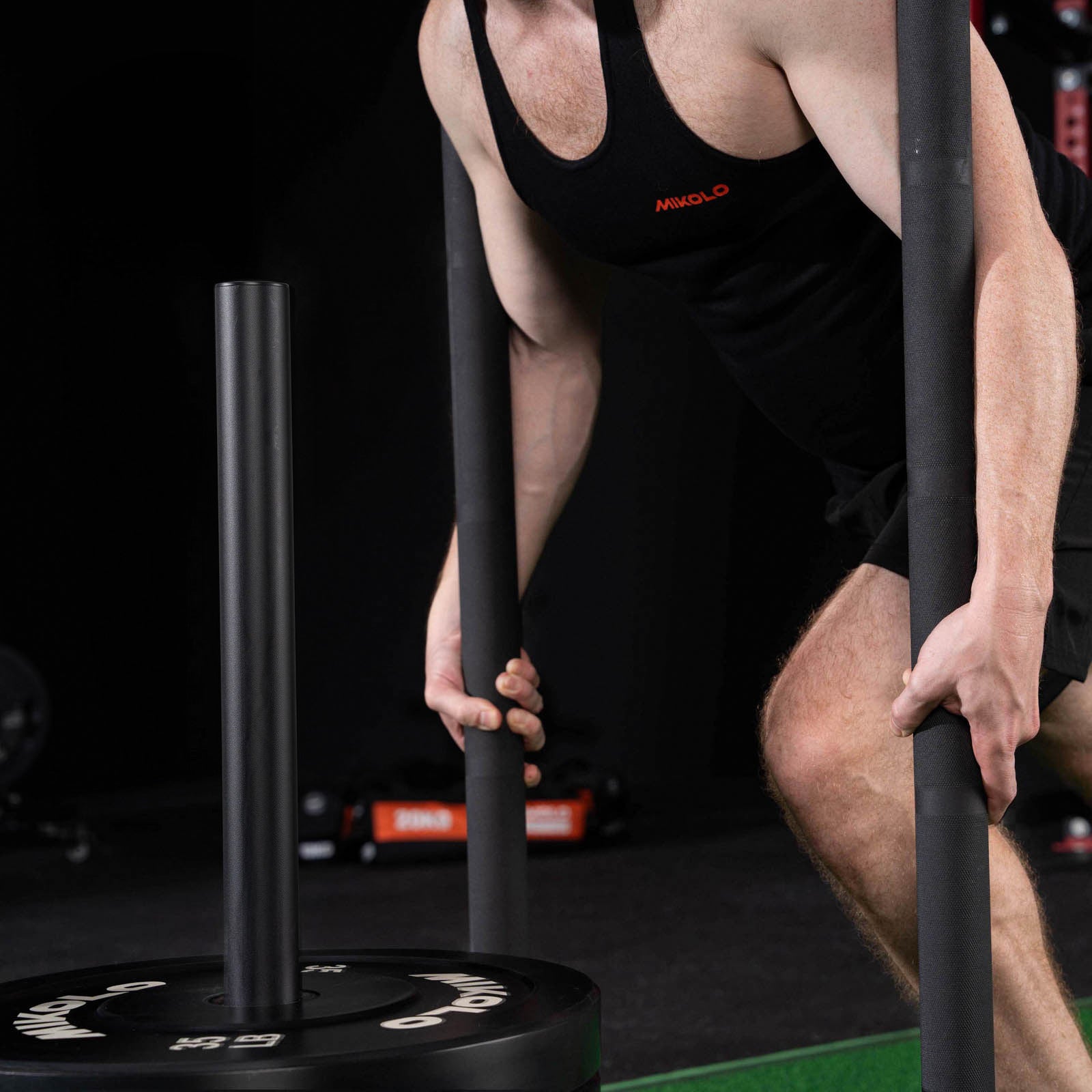 A man grips the vertical handles of a black weighted sled loaded with a 35 lb Mikolo weight plate
