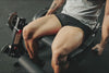 Muscular person sitting on a leg extension machine wearing black shorts and a grey shirt